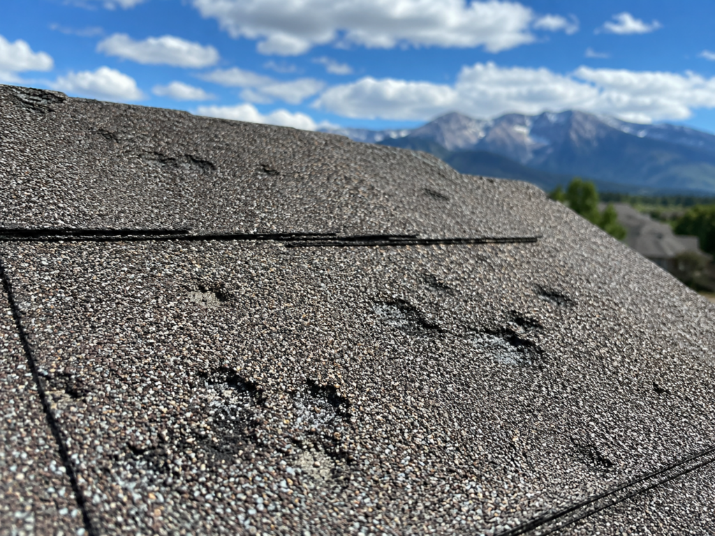 AI-generated image of a close-up shingle with visible hail dents and granule loss, ideally with a Colorado sky in background.